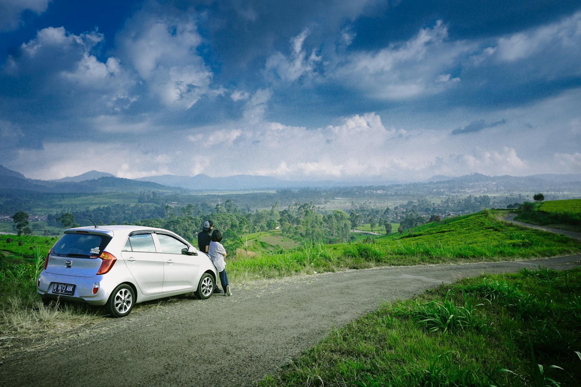 Para przy zaparkowanym aucie z widokiem na zielone pola i pagórki