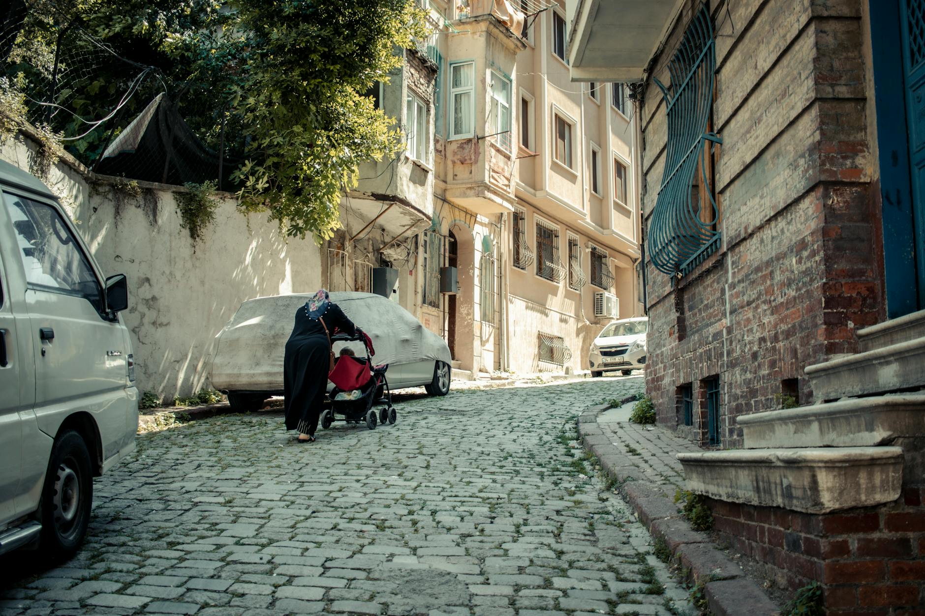 Kobieta z wózkiem spaceruje brukowaną ulicą w słonecznej dzielnicy Lubonia
