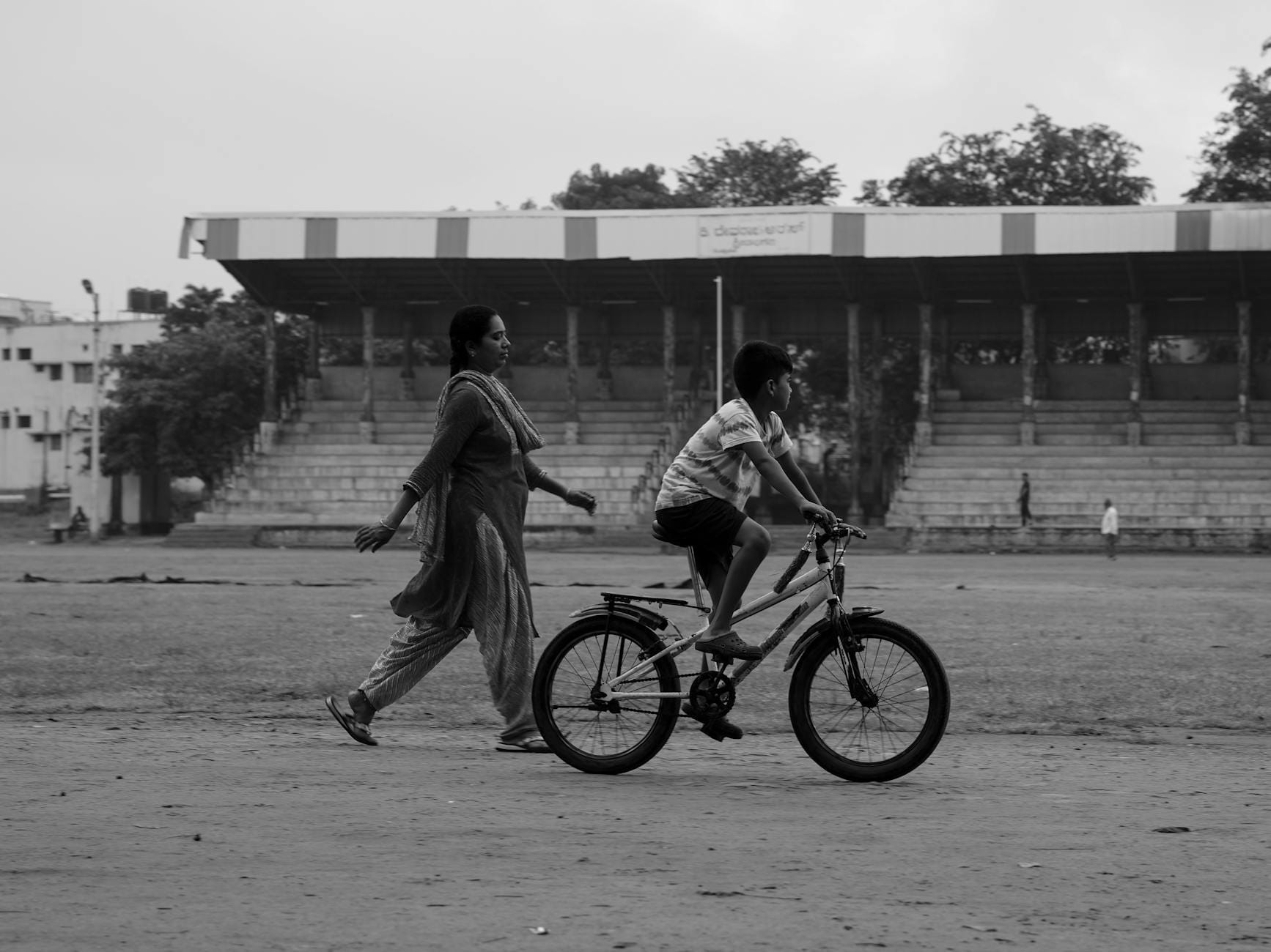 Mama idzie obok syna jadącego na rowerze po parkowej alejce