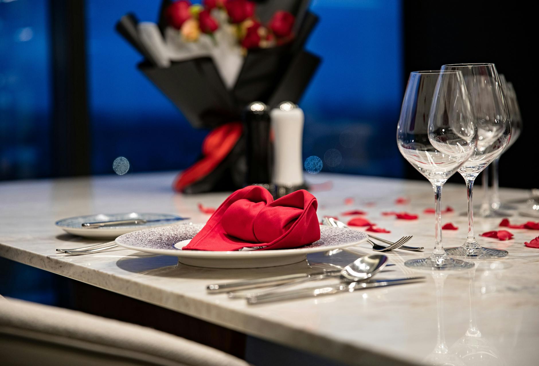 Romantycznie nakryty stół z płatkami czerwonych róż na kolację