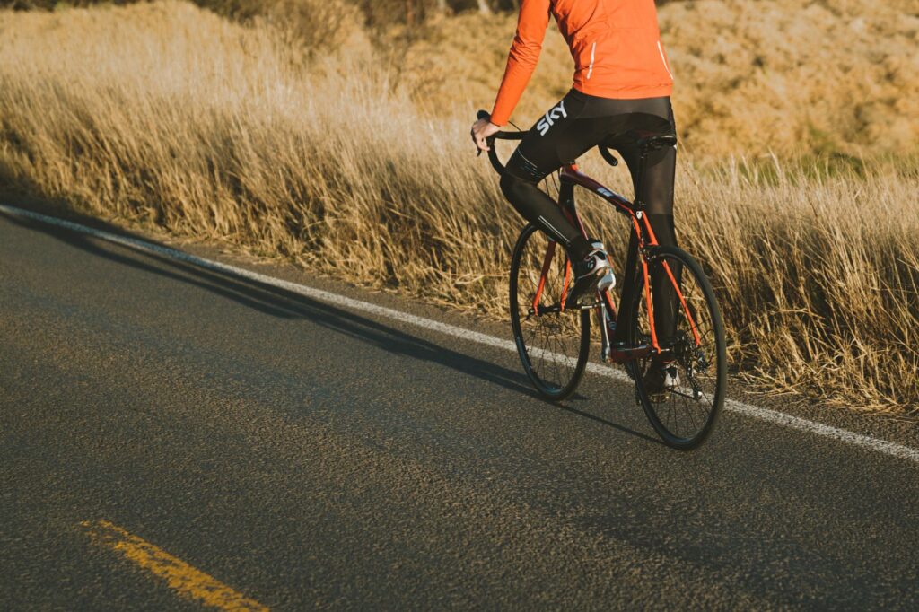 Rowerzysta na szosowym rowerze jedzie słoneczną ścieżką wśród zieleni
