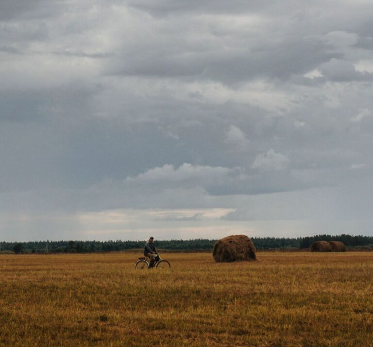 Samotny rowerzysta na wiejskiej drodze wśród pól i stogów siana